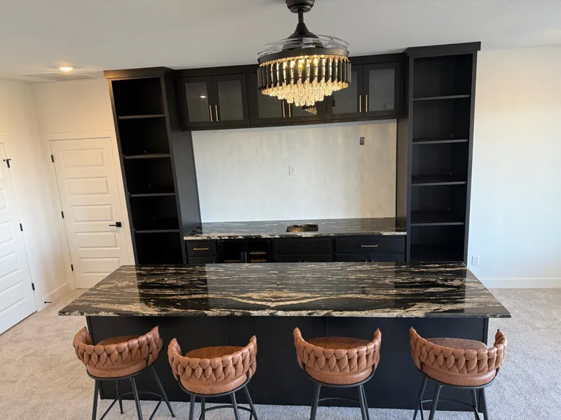 Black built-in bar wall with glass-front cabinets and a granite island, Dripping Springs-area remodel by RenovatePros