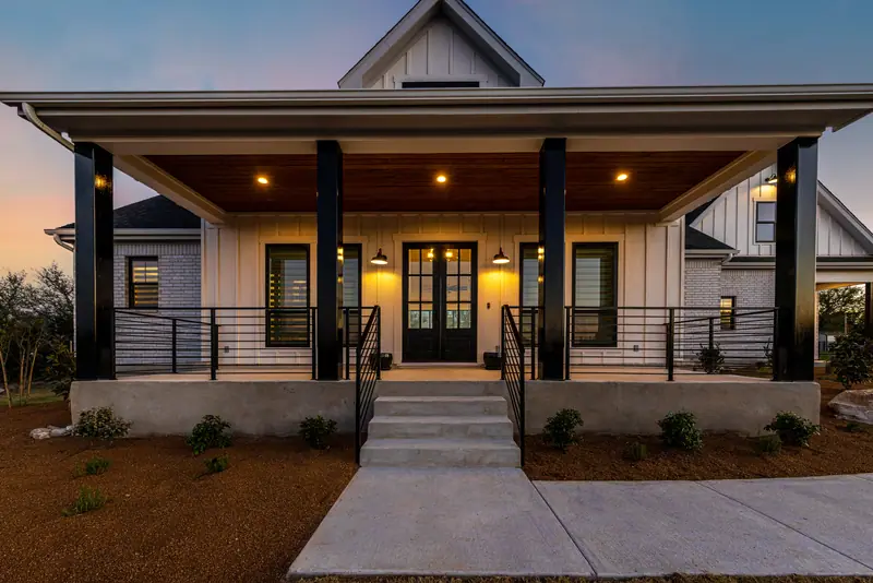 Front porch at dusk with the lights on and a black double door, Farmhouse Hill Country Retreat (RenovatePros project)