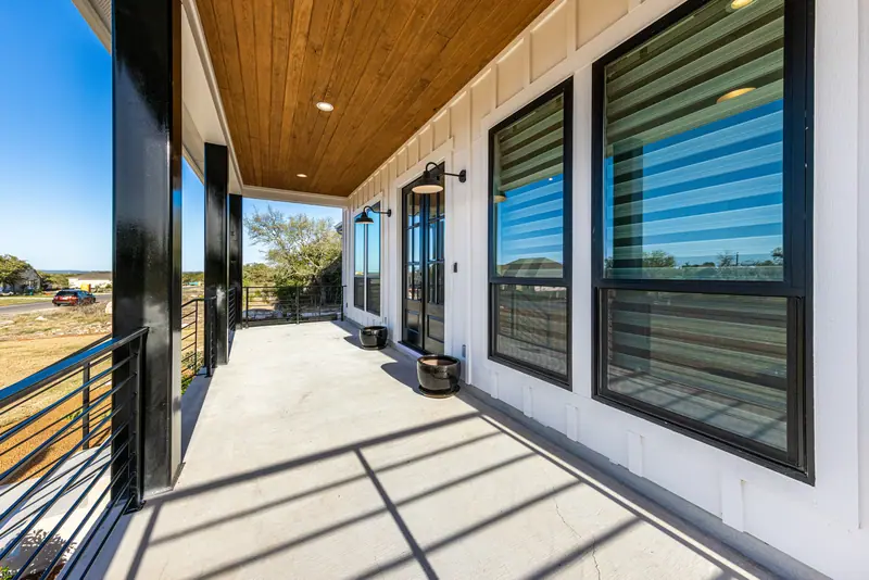 Covered front porch with a wood ceiling and black-framed windows, Farmhouse Hill Country Retreat (RenovatePros project)