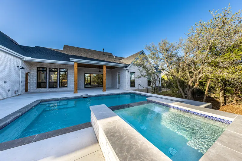 Pool and raised spa behind the house, with oak trees beyond, Farmhouse Hill Country Retreat (RenovatePros project)