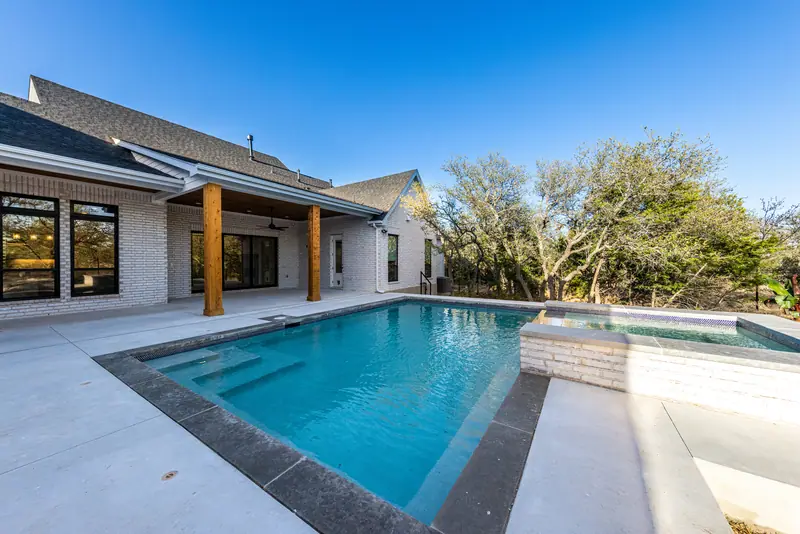 Pool and spa next to the covered back patio, Farmhouse Hill Country Retreat (RenovatePros project)