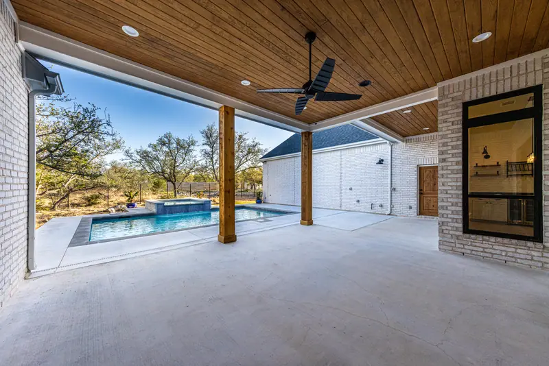 Covered back patio with a wood ceiling and ceiling fan, looking out to the pool, Farmhouse Hill Country Retreat (RenovatePros project)