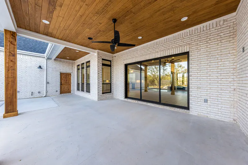 Covered back patio with a wood ceiling and sliding glass doors, Farmhouse Hill Country Retreat (RenovatePros project)