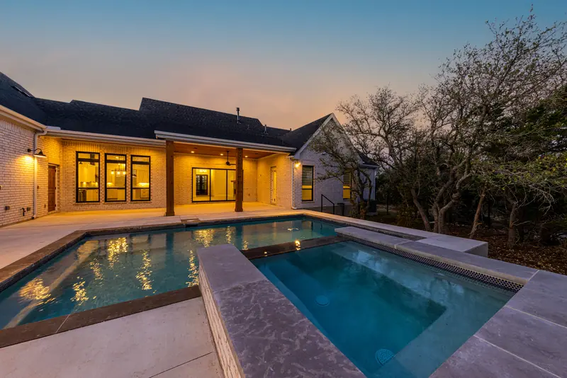 Pool and spa at dusk with the house lit up behind, Farmhouse Hill Country Retreat (RenovatePros project)