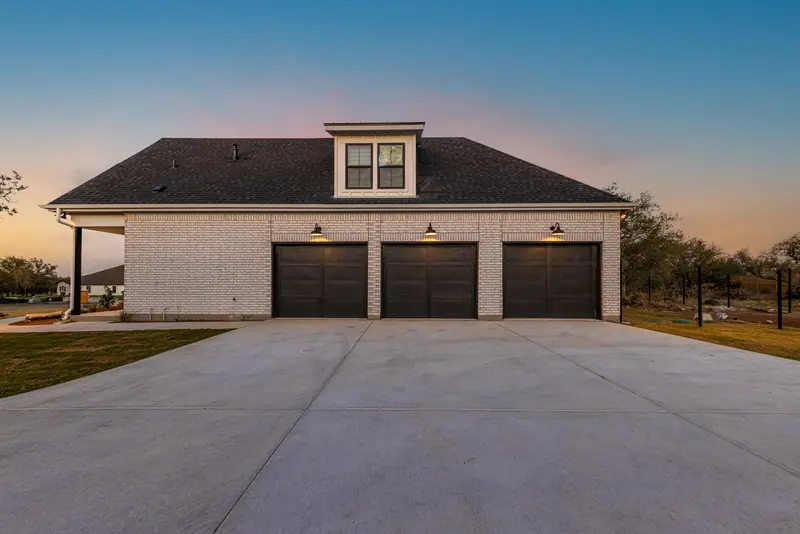 Three-car garage with dark doors at dusk, Farmhouse Hill Country Retreat (RenovatePros project)