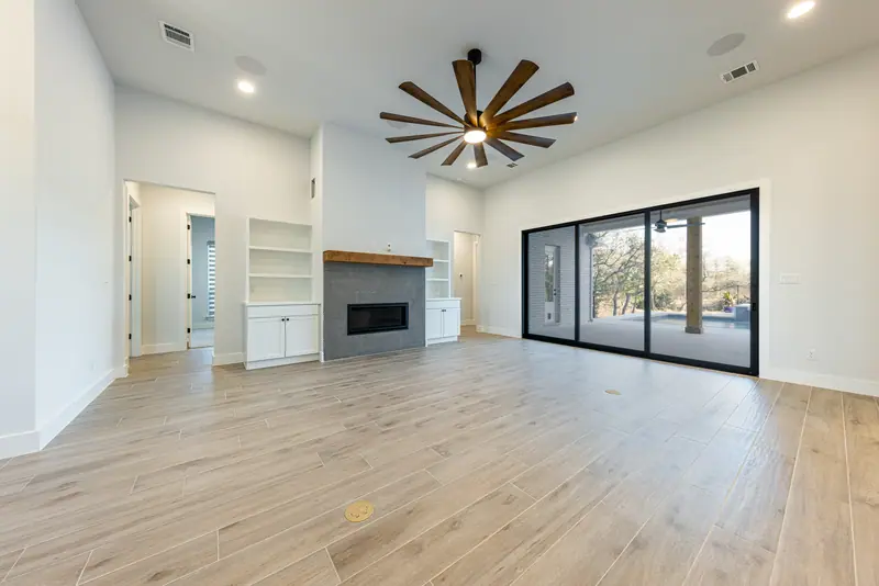 Living room with a tile fireplace, built-in shelves and sliding glass doors, Farmhouse Hill Country Retreat (RenovatePros project)