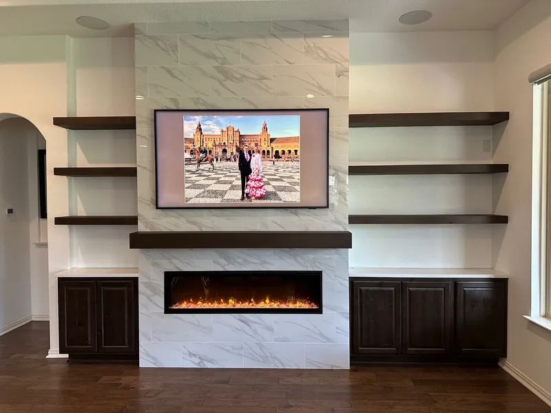 Marble fireplace and TV wall with floating shelves, Living room remodel by RenovatePros