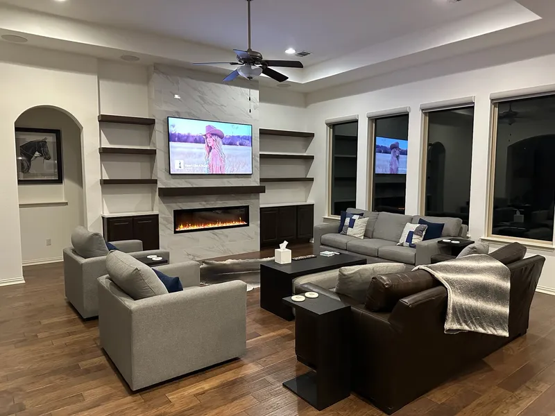 Wide view of a living room with a marble fireplace wall and floating shelves, Living room remodel by RenovatePros