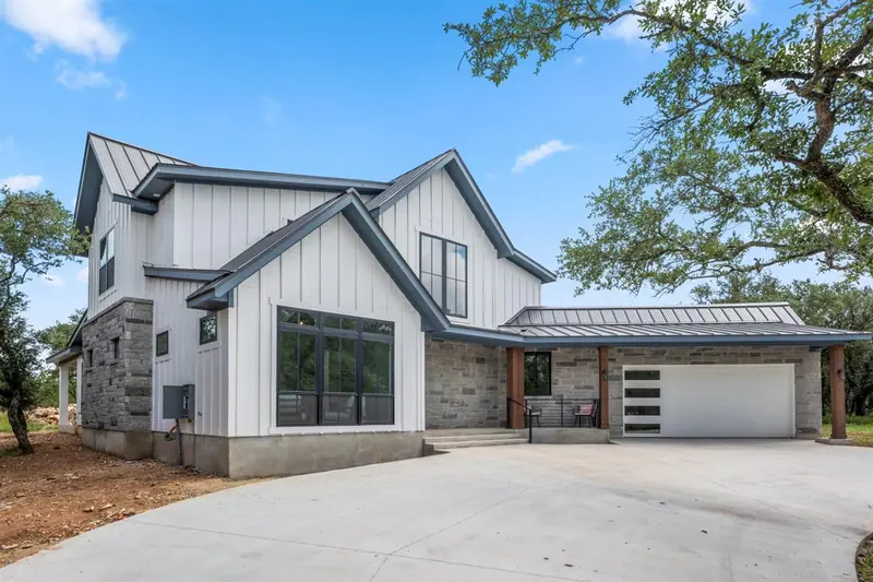 Front of the two-story farmhouse: white board-and-batten siding, a stone base and a two-car garage, Round Mountain Modern Farmhouse (RenovatePros project)