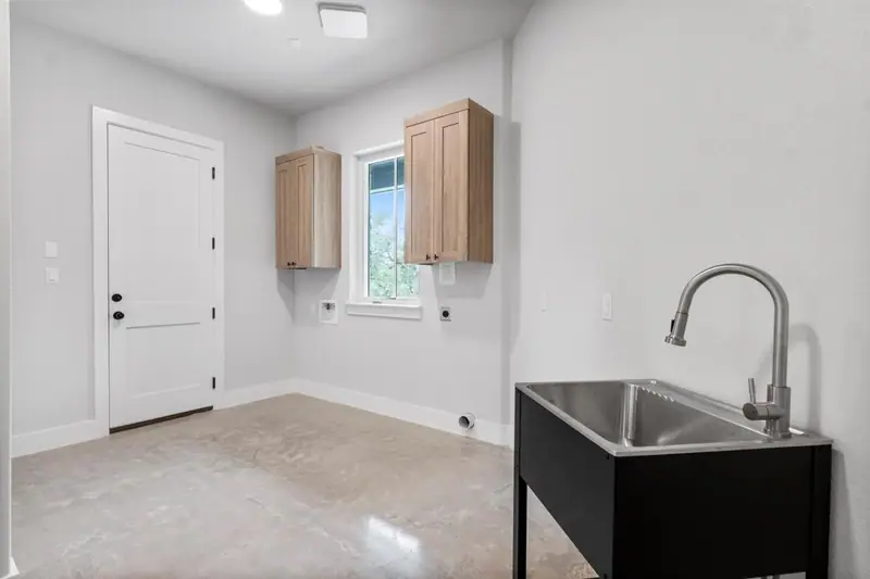 Laundry room with a utility sink and wood-tone upper cabinets, Round Mountain Modern Farmhouse (RenovatePros project)