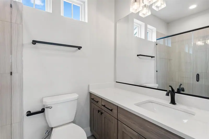 Second bathroom with a wood vanity, white counter and tiled shower, Round Mountain Modern Farmhouse (RenovatePros project)