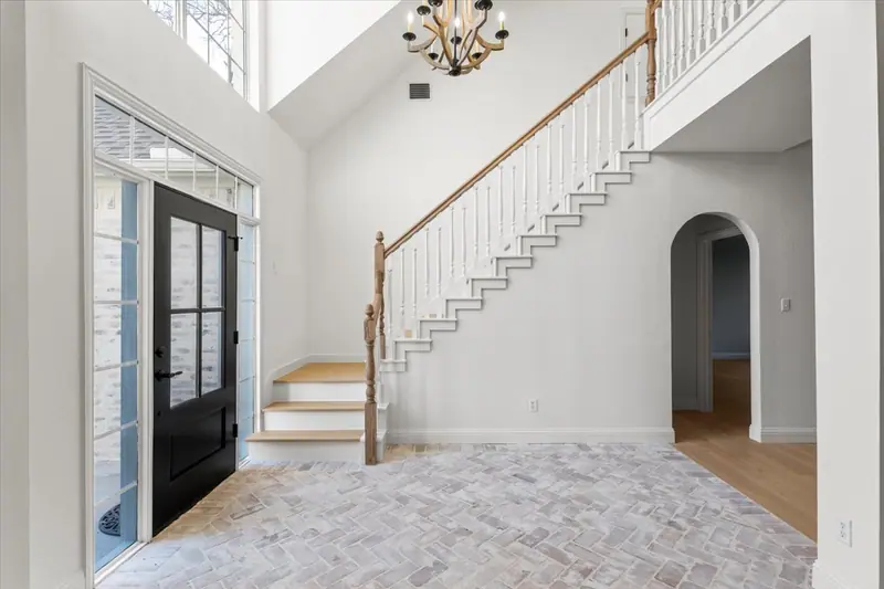 Two-story entry with a black double front door, brick floor and staircase, Round Rock French Country Remodel (RenovatePros project)