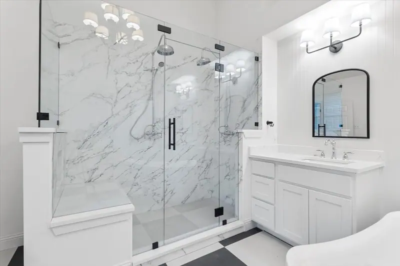 Glass walk-in shower with marble-look walls and a bench, next to a white vanity, Round Rock French Country Remodel (RenovatePros project)