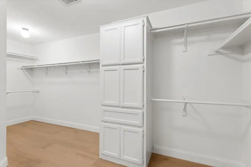 Walk-in closet with hanging rods and a built-in white cabinet tower, Round Rock French Country Remodel (RenovatePros project)