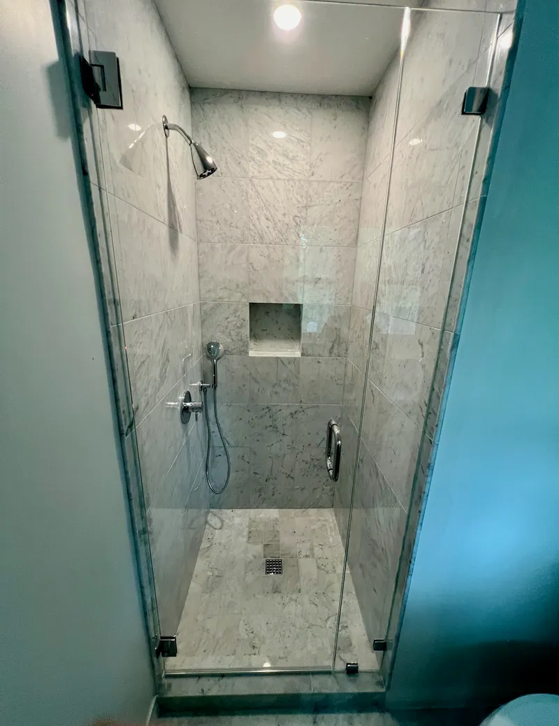 Marble walk-in shower with frameless glass, Westlake-area remodel by RenovatePros