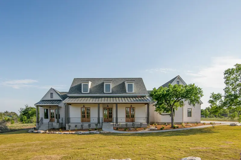 Front of the home in daylight: white brick, dormers, a metal porch roof and wood doors, Spicewood Modern Farmhouse (RenovatePros project)