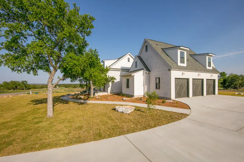 Three-car garage with a curved driveway and a large shade tree, Spicewood Modern Farmhouse (RenovatePros project)
