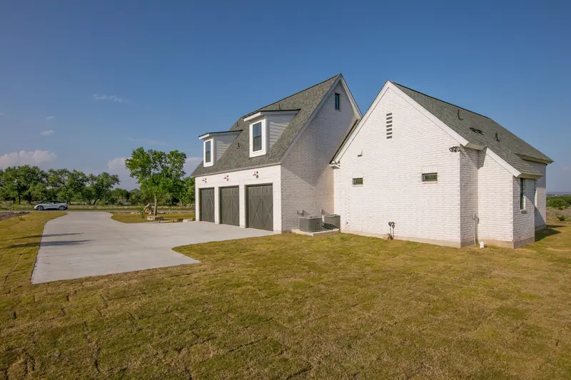 Garage side of the white brick home, Spicewood Modern Farmhouse (RenovatePros project)