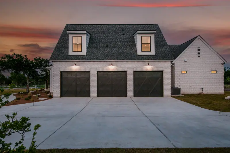 Three-car garage at dusk with the lights on, Spicewood Modern Farmhouse (RenovatePros project)