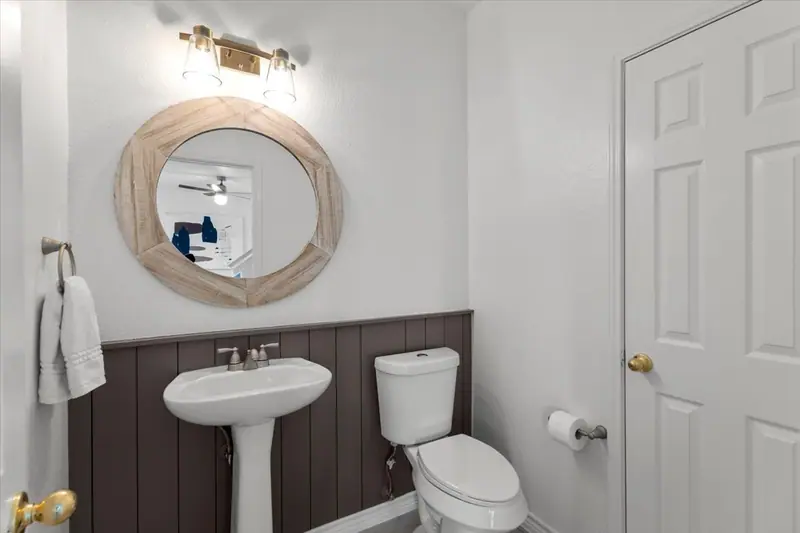 Half bath with dark board-and-batten wainscot, a pedestal sink and a round mirror, Two-Story Home Remodel, 2026 (RenovatePros project)