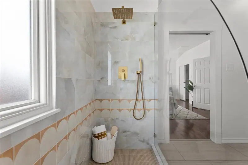 Shower with a gold rain head and hand shower, marble-look tile and a scalloped border, Two-Story Home Remodel, 2026 (RenovatePros project)